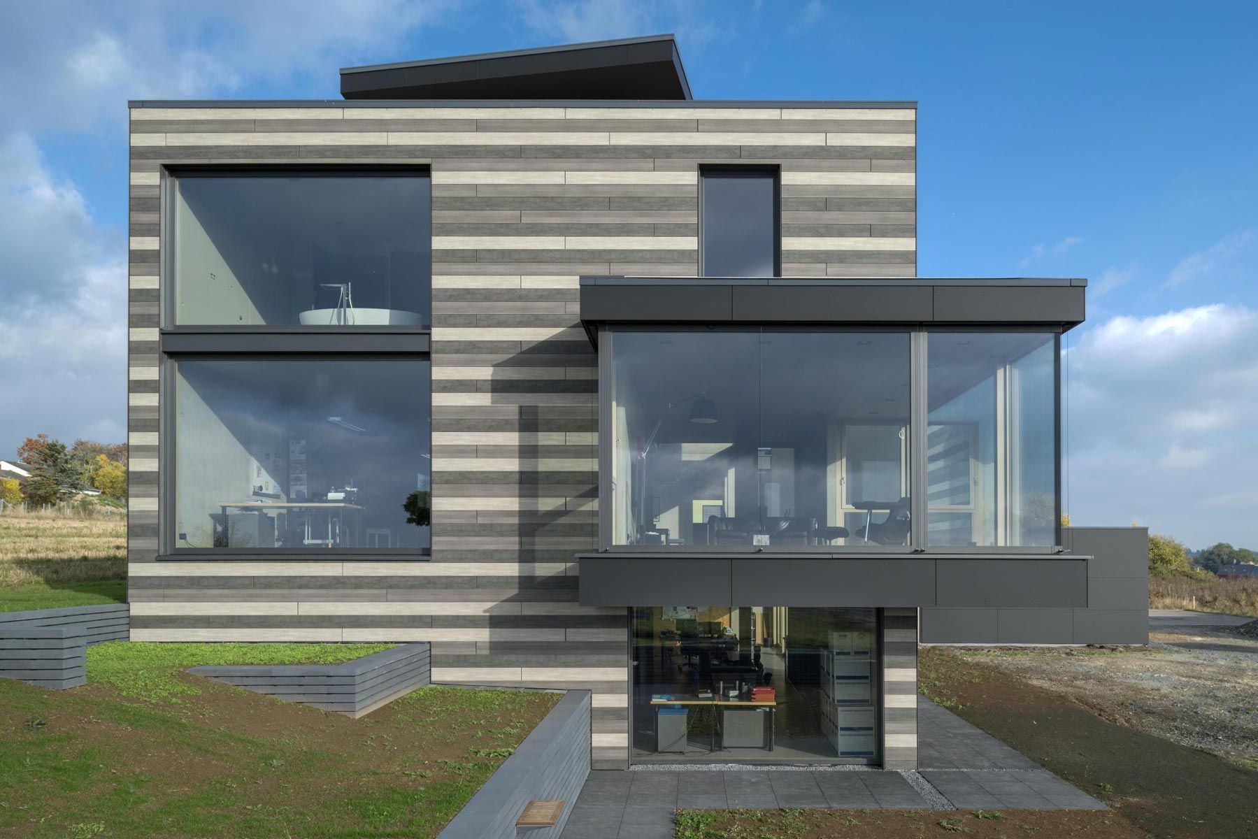 Modernes Objekt mit einem Anbau und einer großen Glasfläche. Die Fassade wurde mit Paneelen in unterschiedlichen Farben versehen.